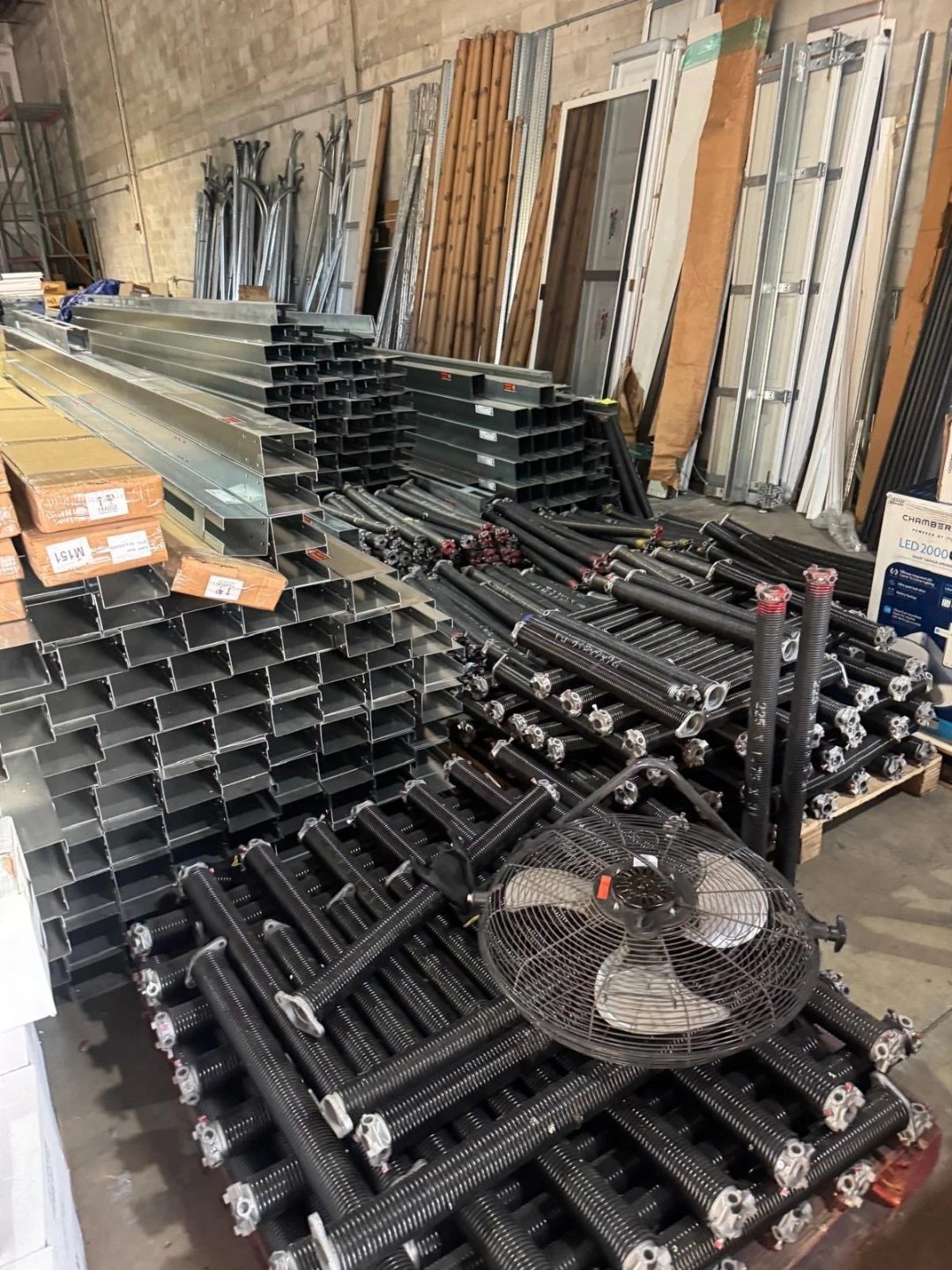 Racks of steel track sections and black torsion springs stacked in a parts room