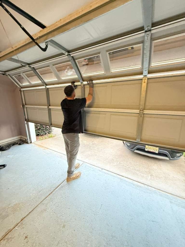 Technician checking a sectional door raised partway with a parked car beyond it