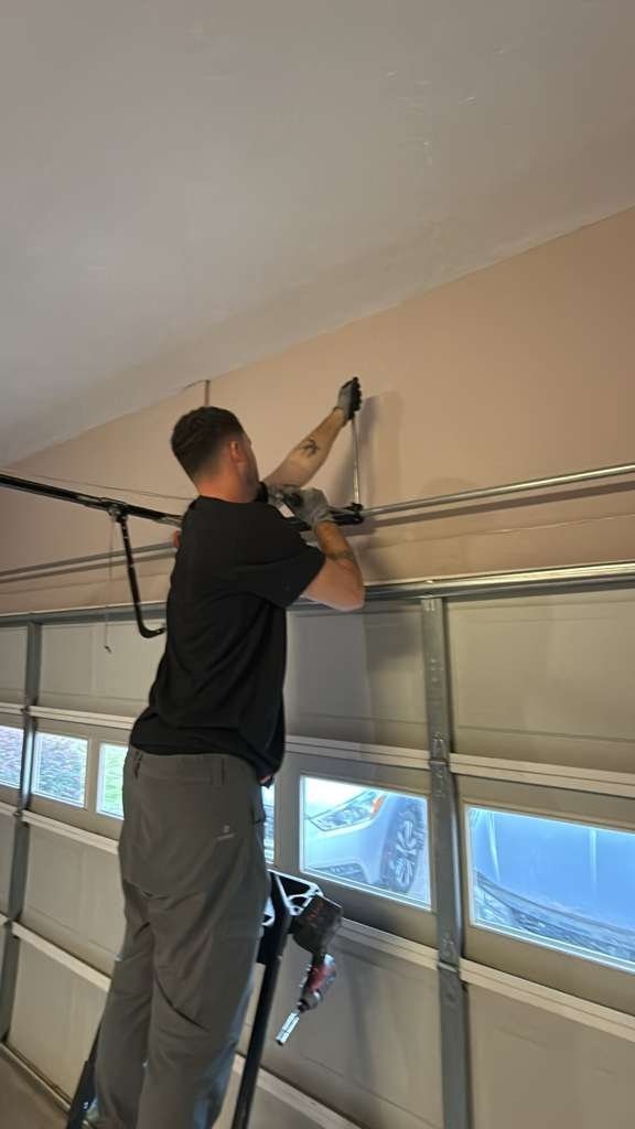 Technician on a short ladder fitting hardware above a door with a row of window panels