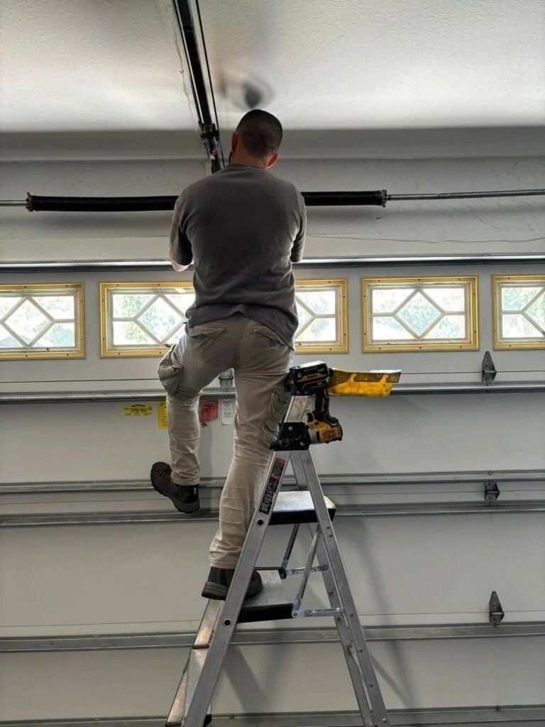 Technician on a stepladder with a drill beside him, working near the top of a window-panel door