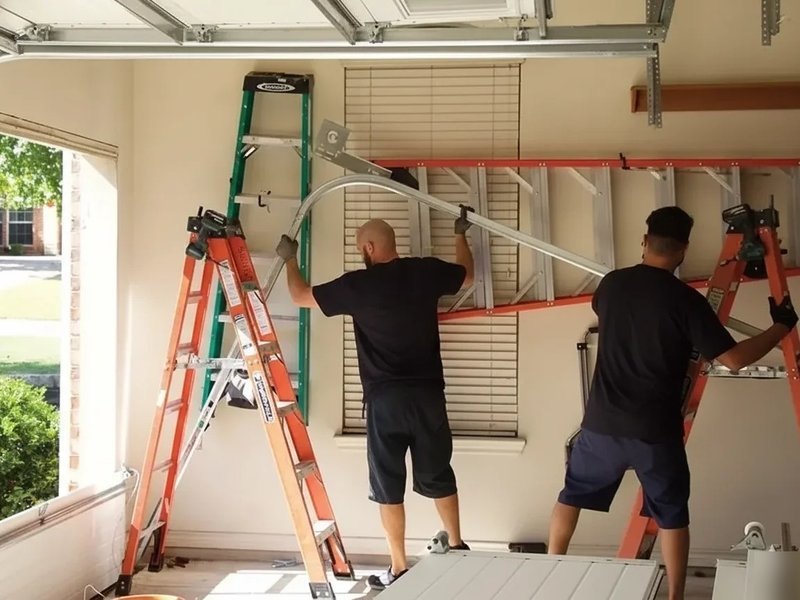 Two technicians with a ladder at an open garage at dusk