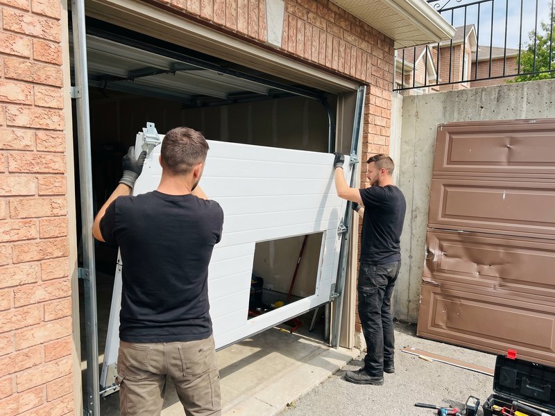 Two technicians lifting a new panel into a garage door