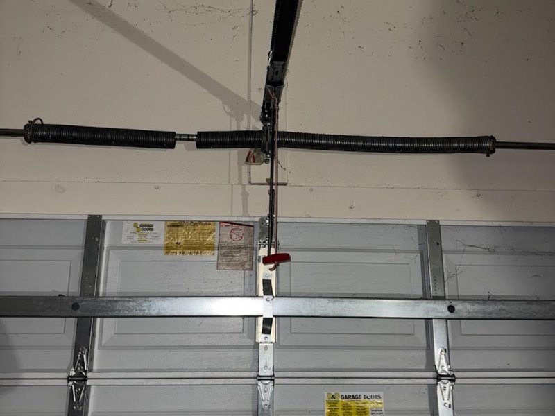 Black torsion spring on its shaft above the top panel of a closed garage door
